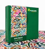 A green jigsaw puzzle box with a colorful Arabic calligraphy pattern on the front, labeled 'PUZZLERS' and '500 PIECE JIGSAW PUZZLE,' standing on a patterned surface against a white background.